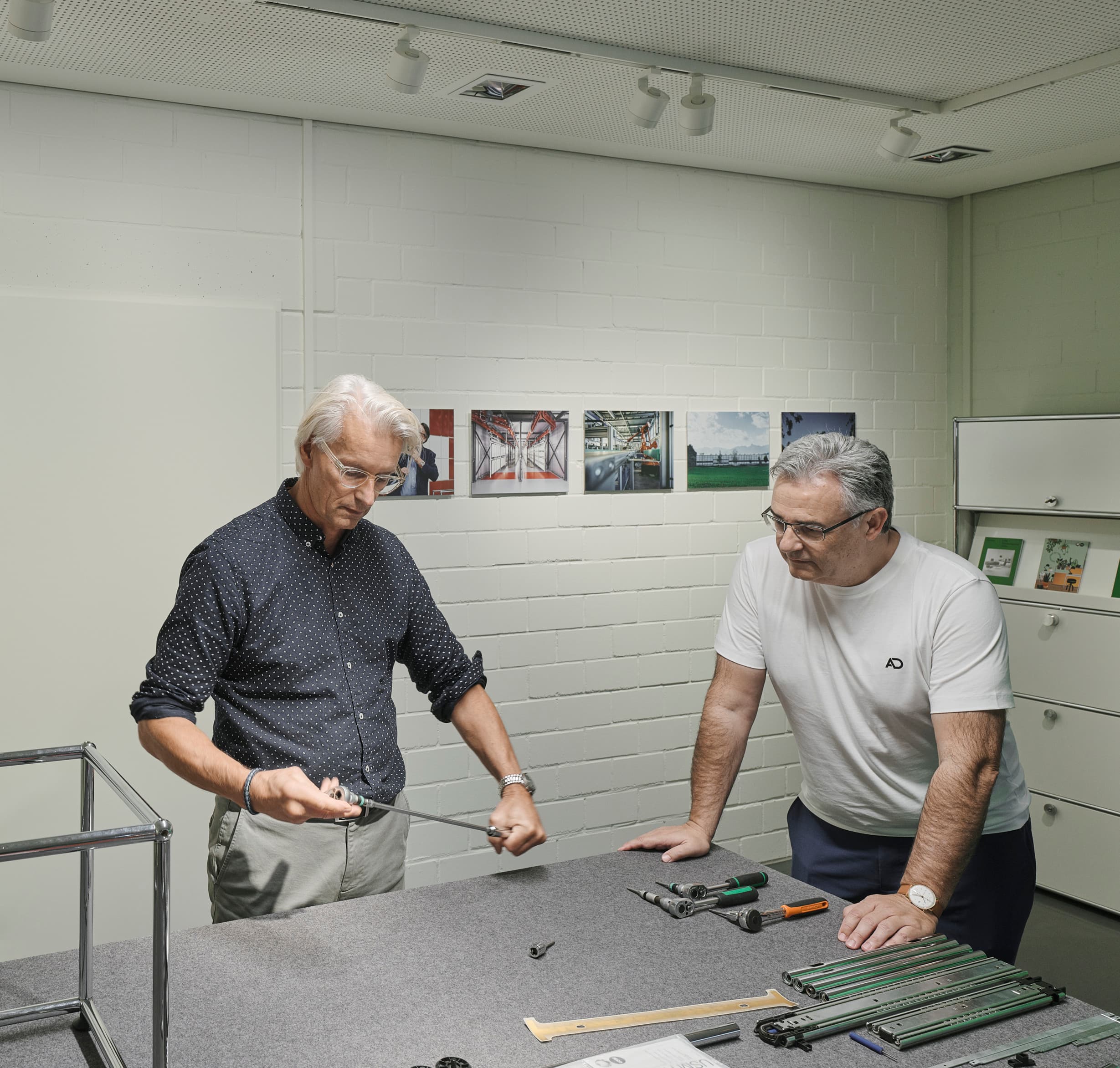 USM Show Office: Zwei Personen montieren USM Möbel unter ERCO Track Downlights für flexible Bürobeleuchtung.