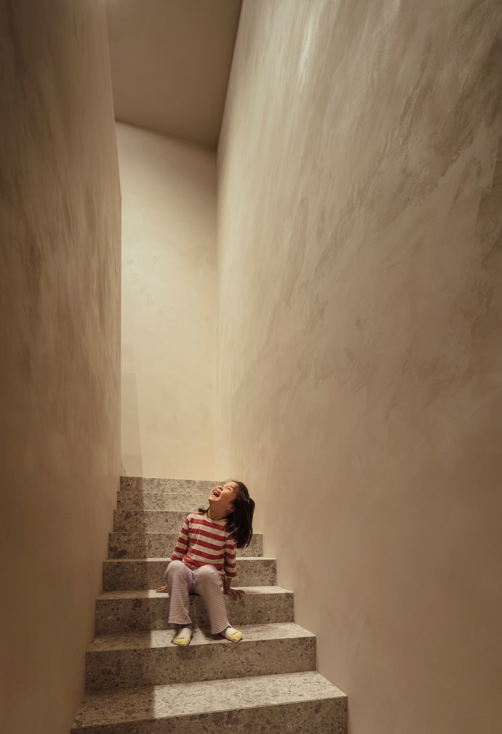 Mädchen sitzt auf Treppe in Daisy Home, beleuchtet mit ERCO Lichtlösung für angenehme Atmosphäre.
