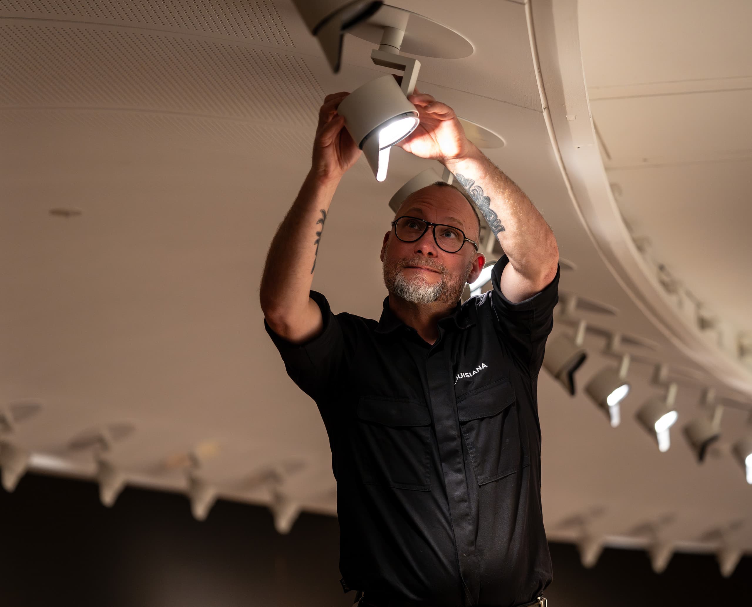 Ein Mann justiert einen ERCO Parscan LED-Strahler im Louisiana Museum, um die Ausstellungsbeleuchtung zu optimieren.