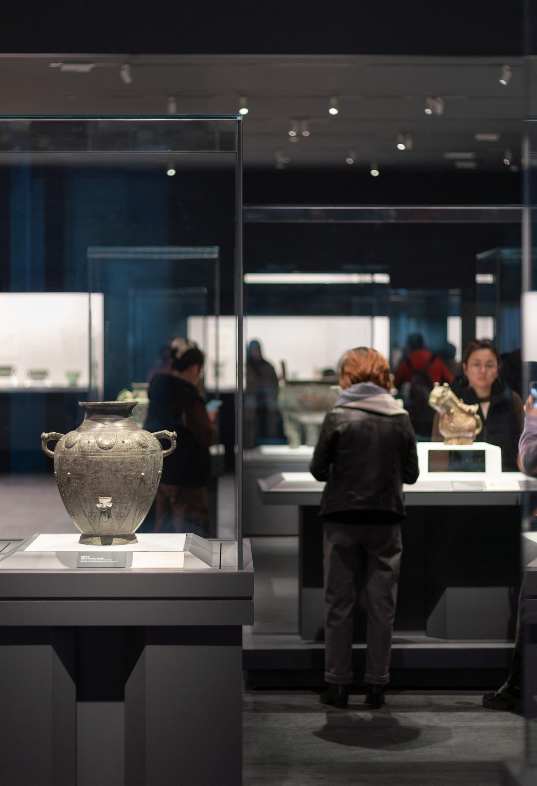 Besucher betrachten beleuchtete Bronzegefäße im Shanghai Museum East, ausgestellt mit ERCO Strahlern.