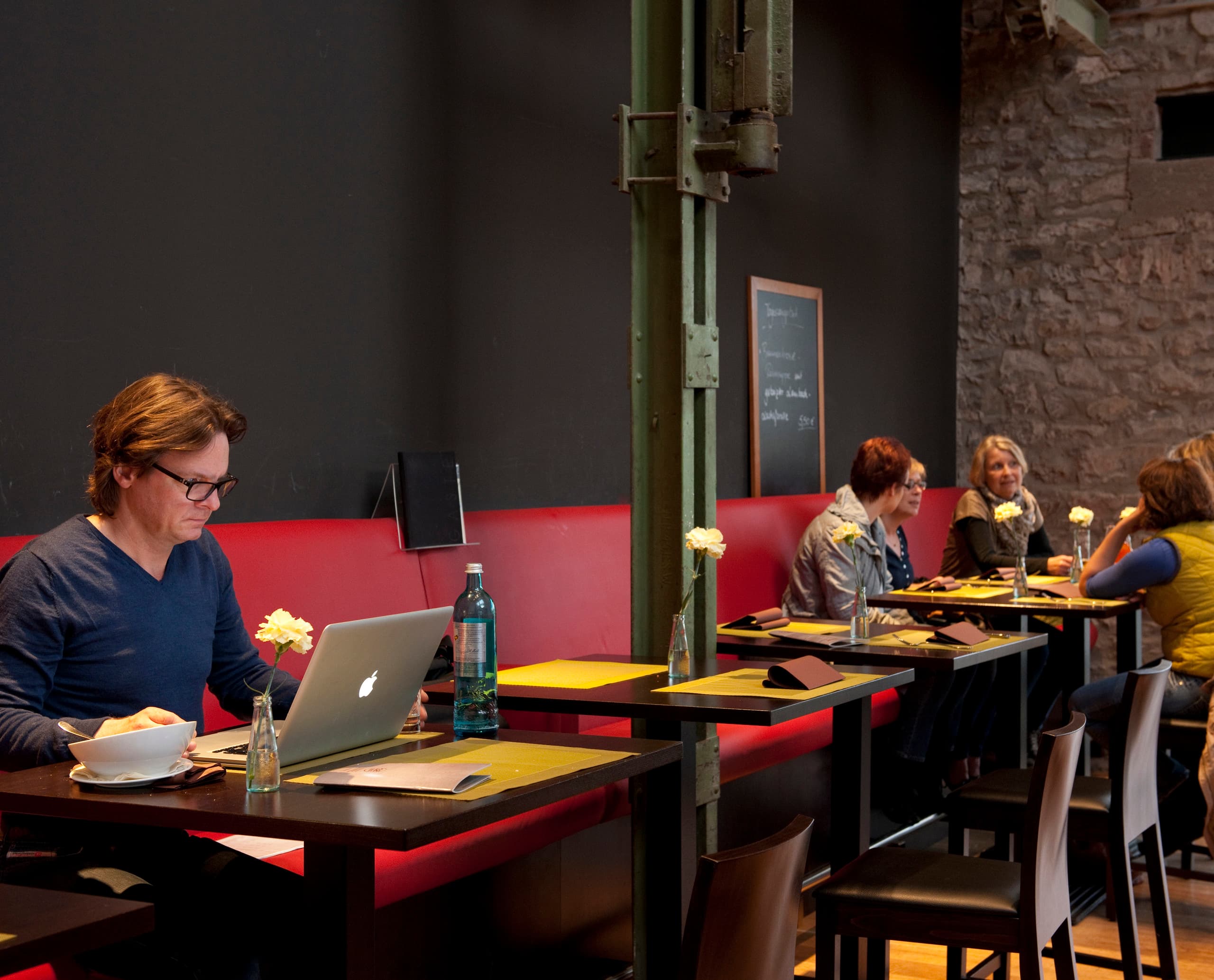 Gast im Halle 32 Restaurant in Gummersbach mit Laptop an einem Tisch. Industrielles Ambiente mit ERCO Beleuchtung.