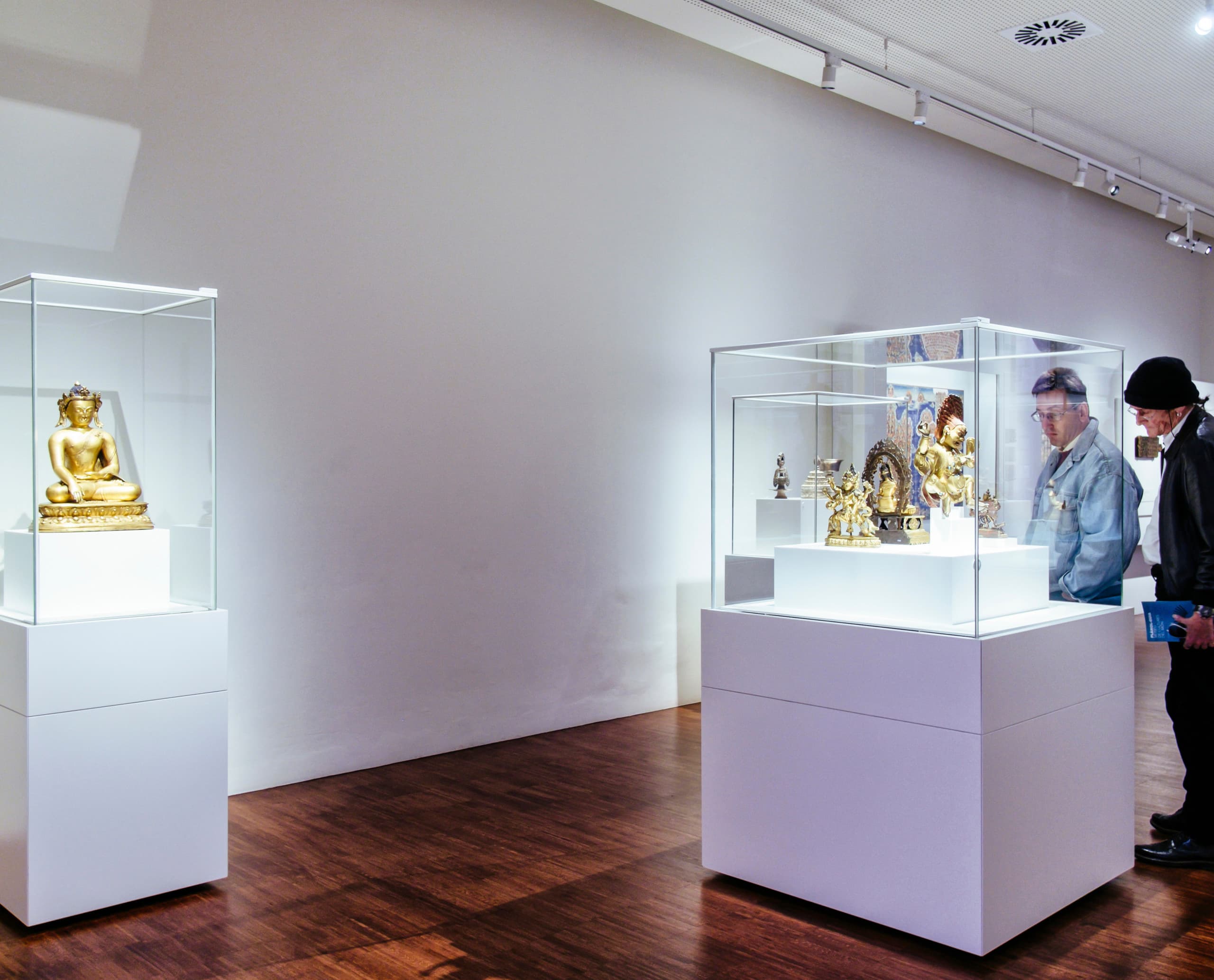 Besucher betrachten Buddha-Statuen in Vitrinen, beleuchtet mit ERCO Optec Strahlern im Museu de Cultures del Món, Barcelona.