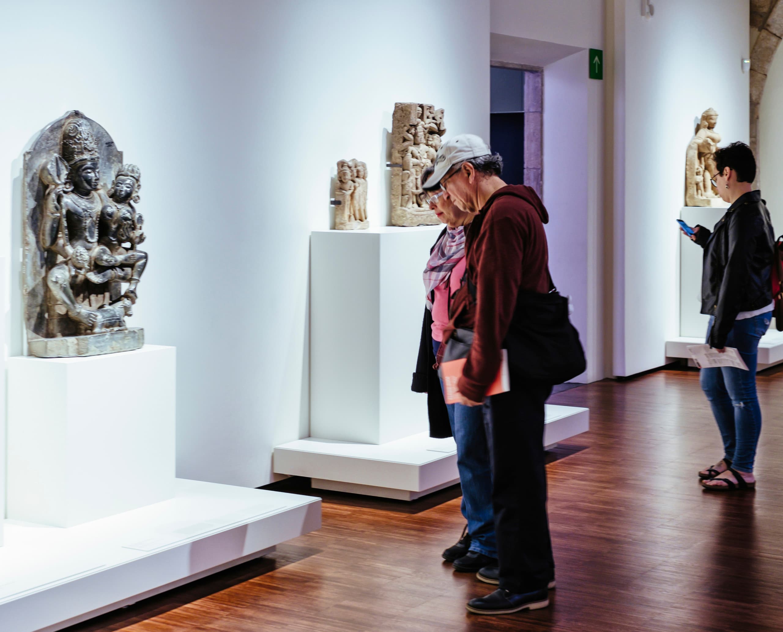 Besucher betrachten Skulpturen im Museu de Cultures del Món, beleuchtet mit ERCO Optec Strahlern.