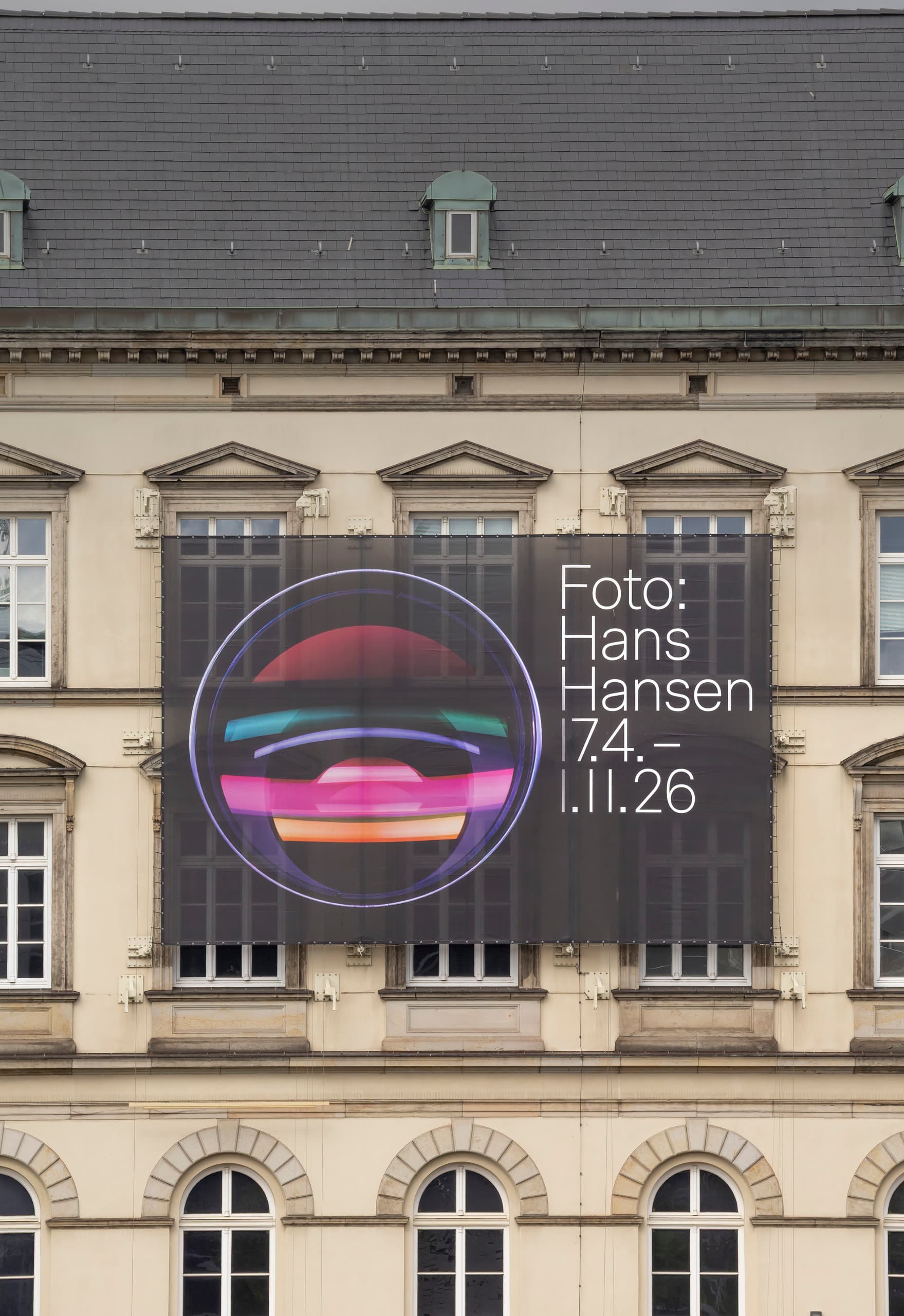 Plakat mit Werbung für eine Ausstellung an Fassadenwand.