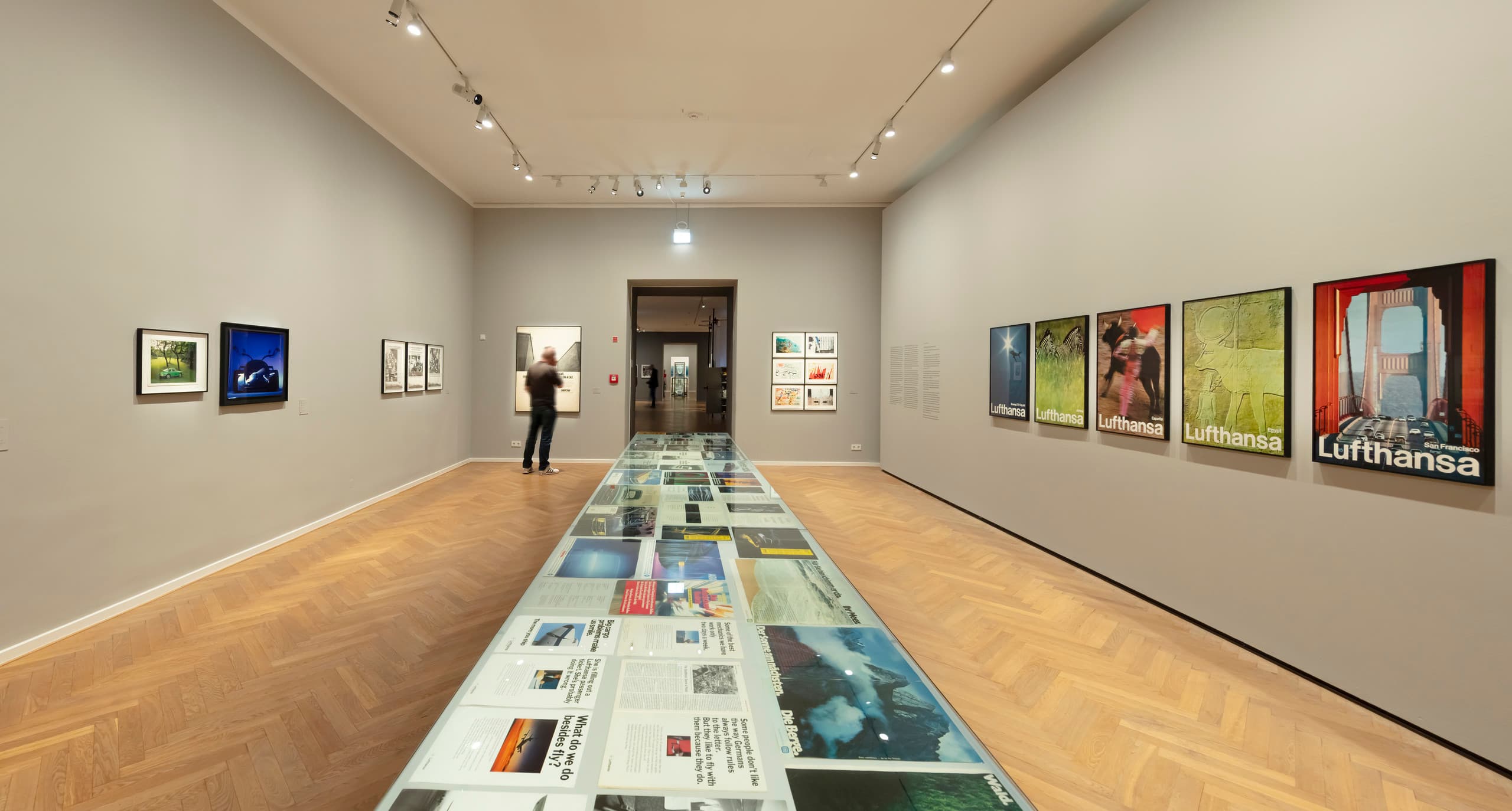 Ausstellungsraum mit Bildern an grauen Wänden und Präsentationstisch mittig.