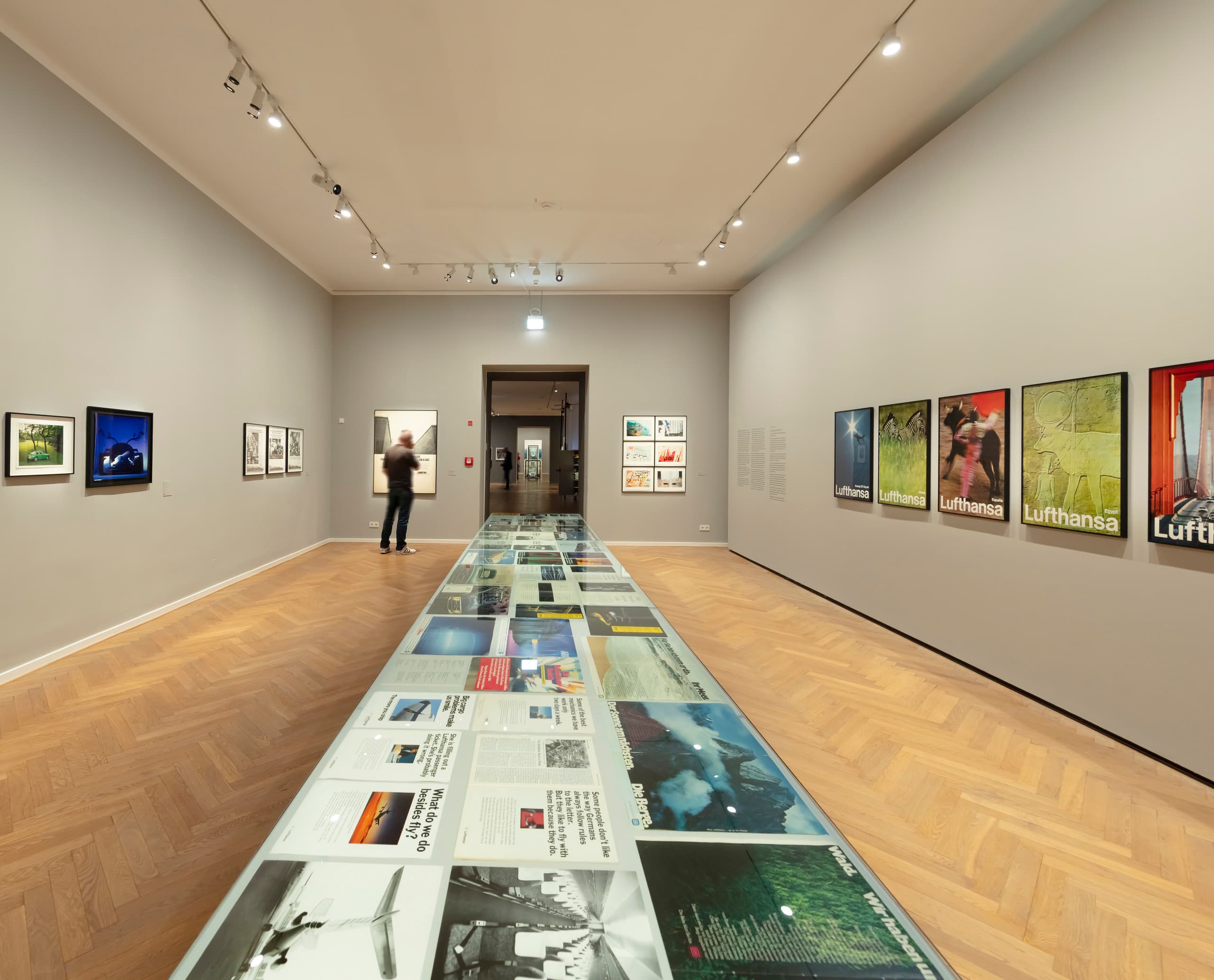 Ausstellungsraum mit Bildern an grauen Wänden und Präsentationstisch mittig.