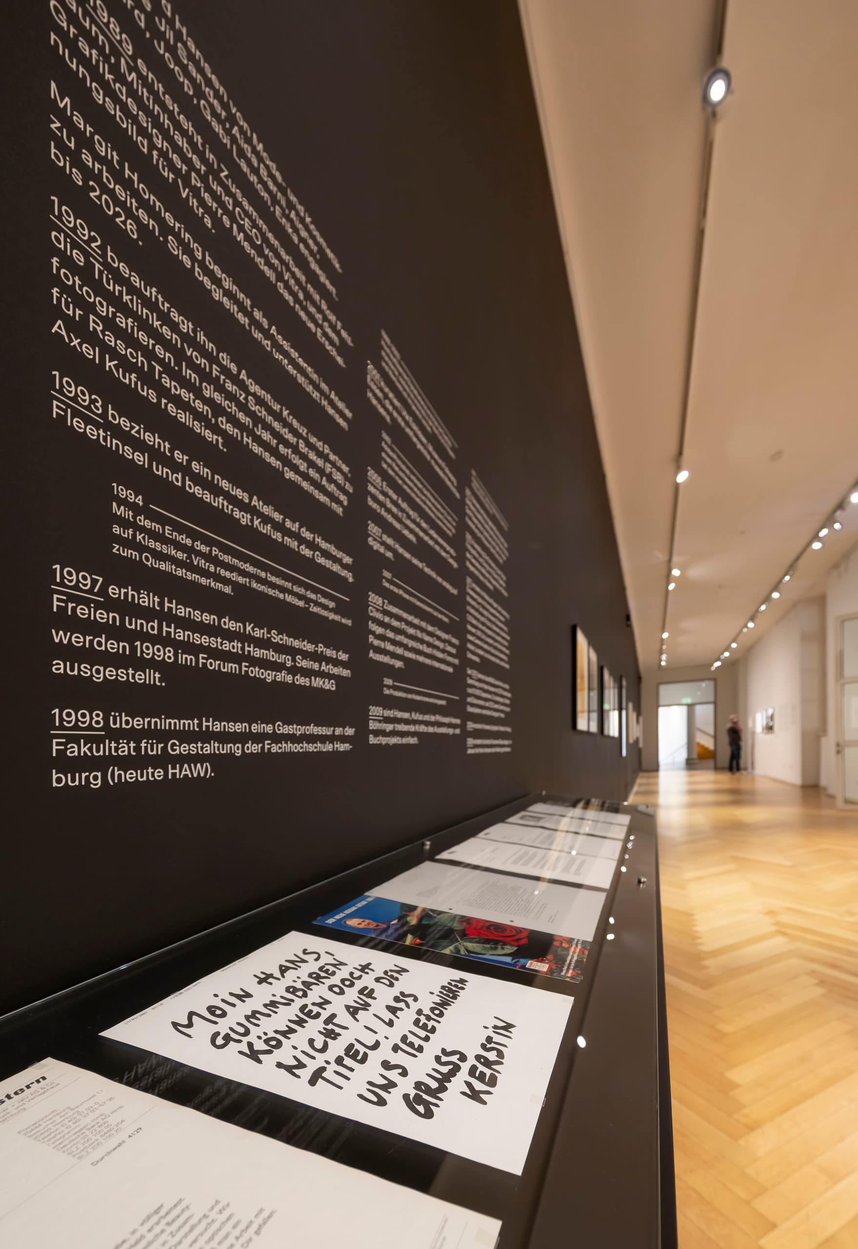 Gang, links schwarze Wand mit Aufschrift und ausgestellten Schriften.