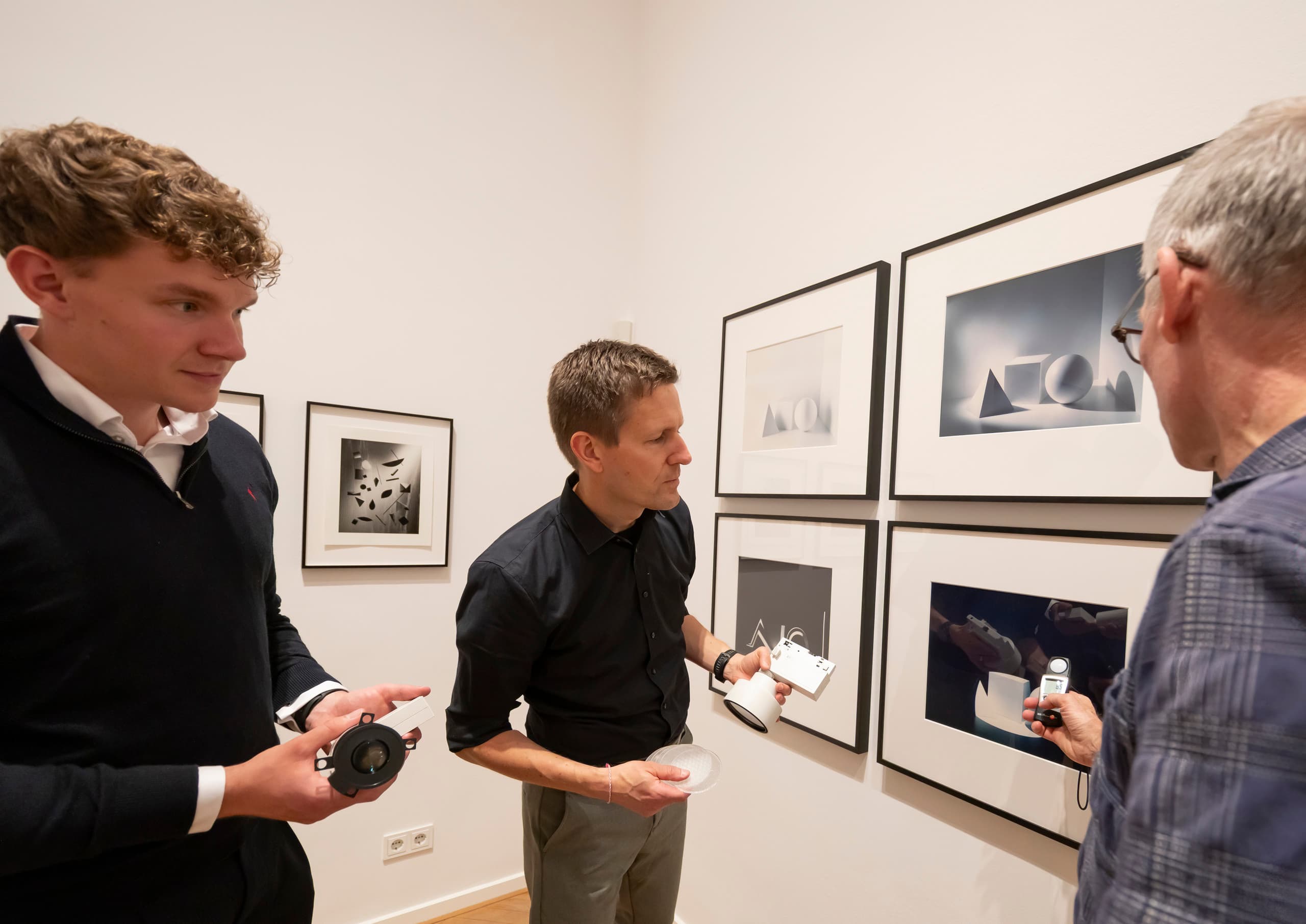 Drei Männer in Ausstellungsraum mit Leuchte in der Hand.