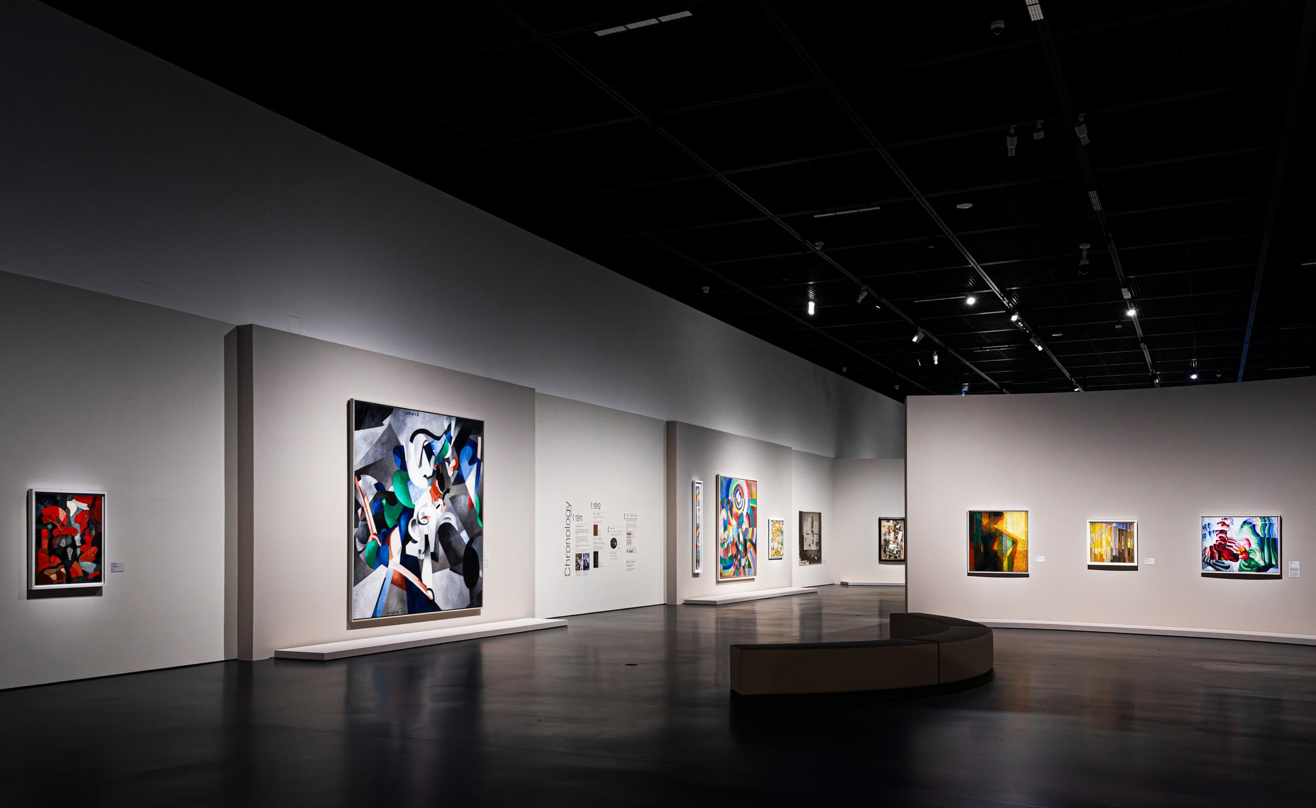 Weißer Ausstellungsraum mit Bildern an den Wänden, schwarzer Decke und schwarzem Boden.
