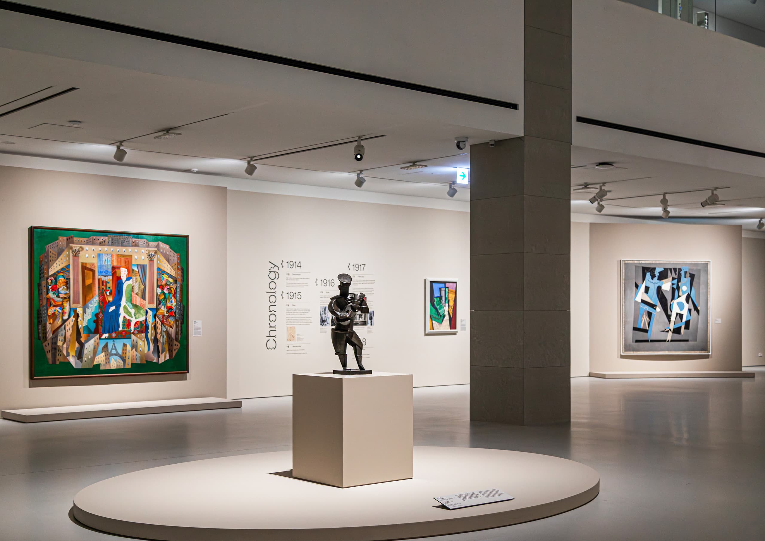 Ausstellungsraum mit vielen Bildern und zentraler Skulptur.