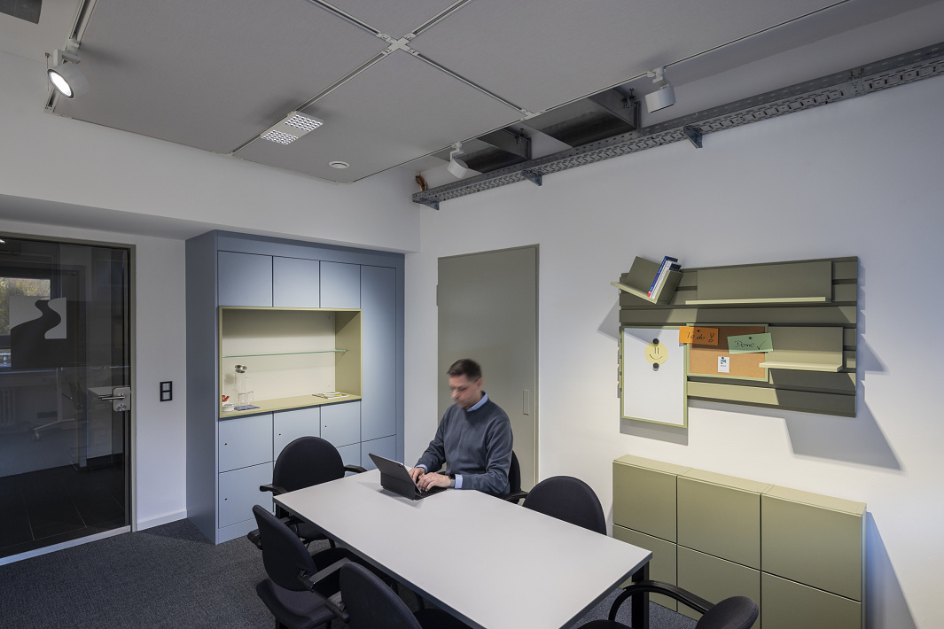 A meeting room in the office featuring a table-based workstation, wall-mounted fixtures and a ceiling track lighting system with flexibly adjustable spotlights for customisable lighting.