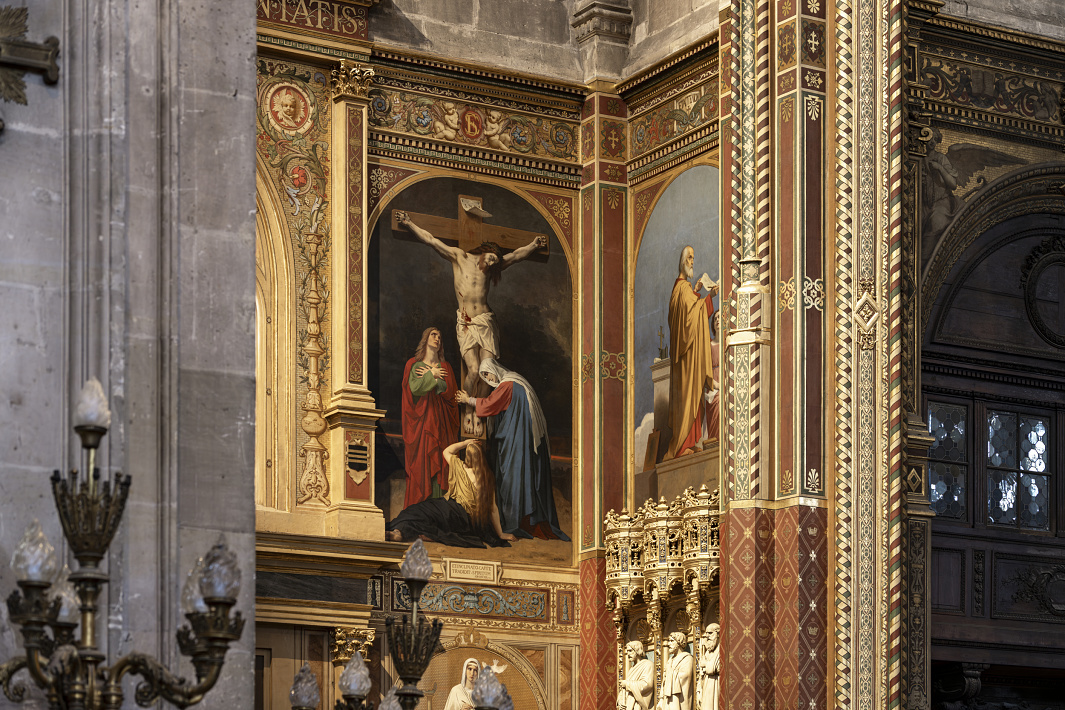 Painted wall panels inside a historic church depicting religious scenes, including a crucifixion set within ornate gold and red architectural framing. The surrounding stone columns, carved details, and decorative borders emphasize the richly adorned interior.